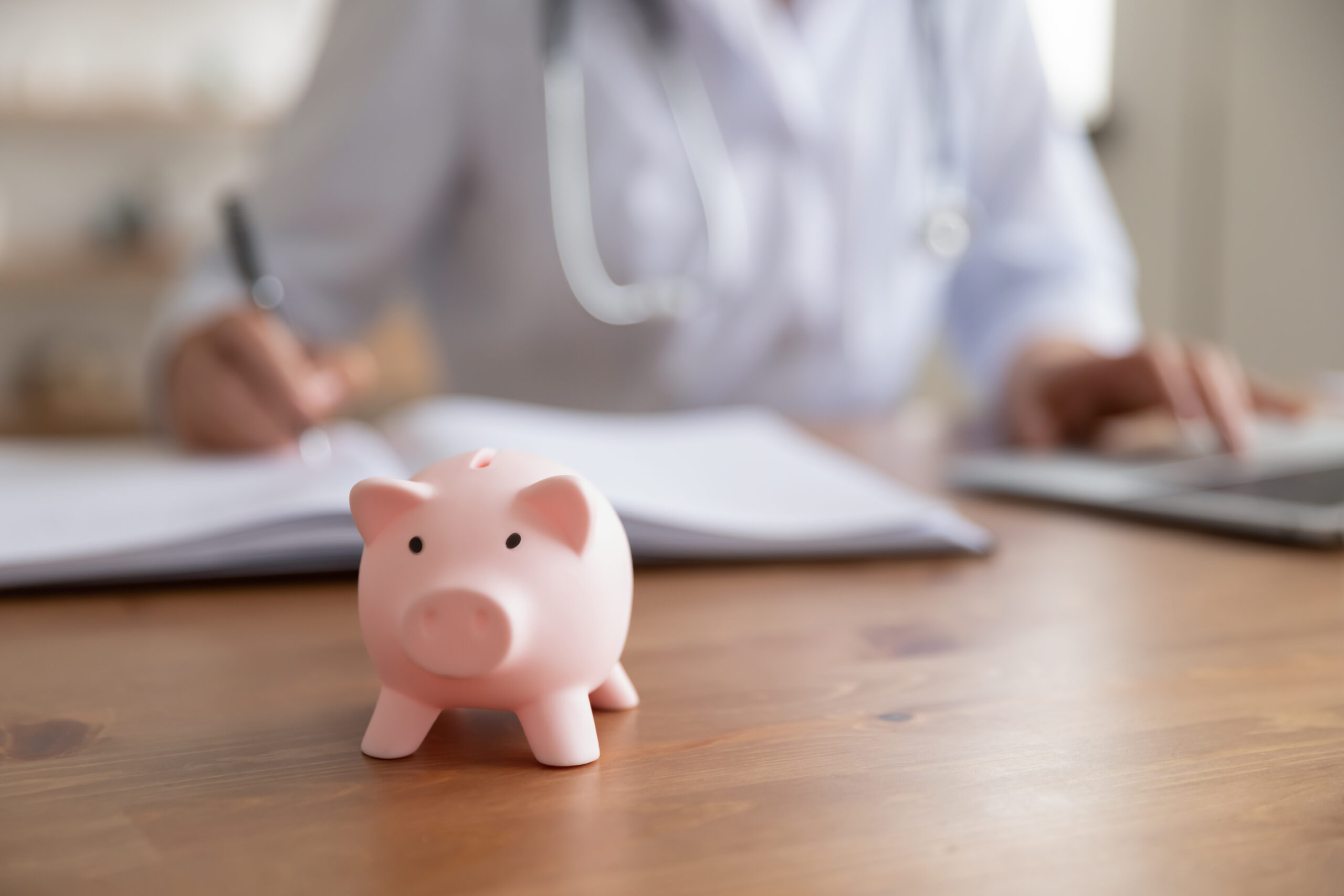 Female doctor working at desk with piggy bank, close up