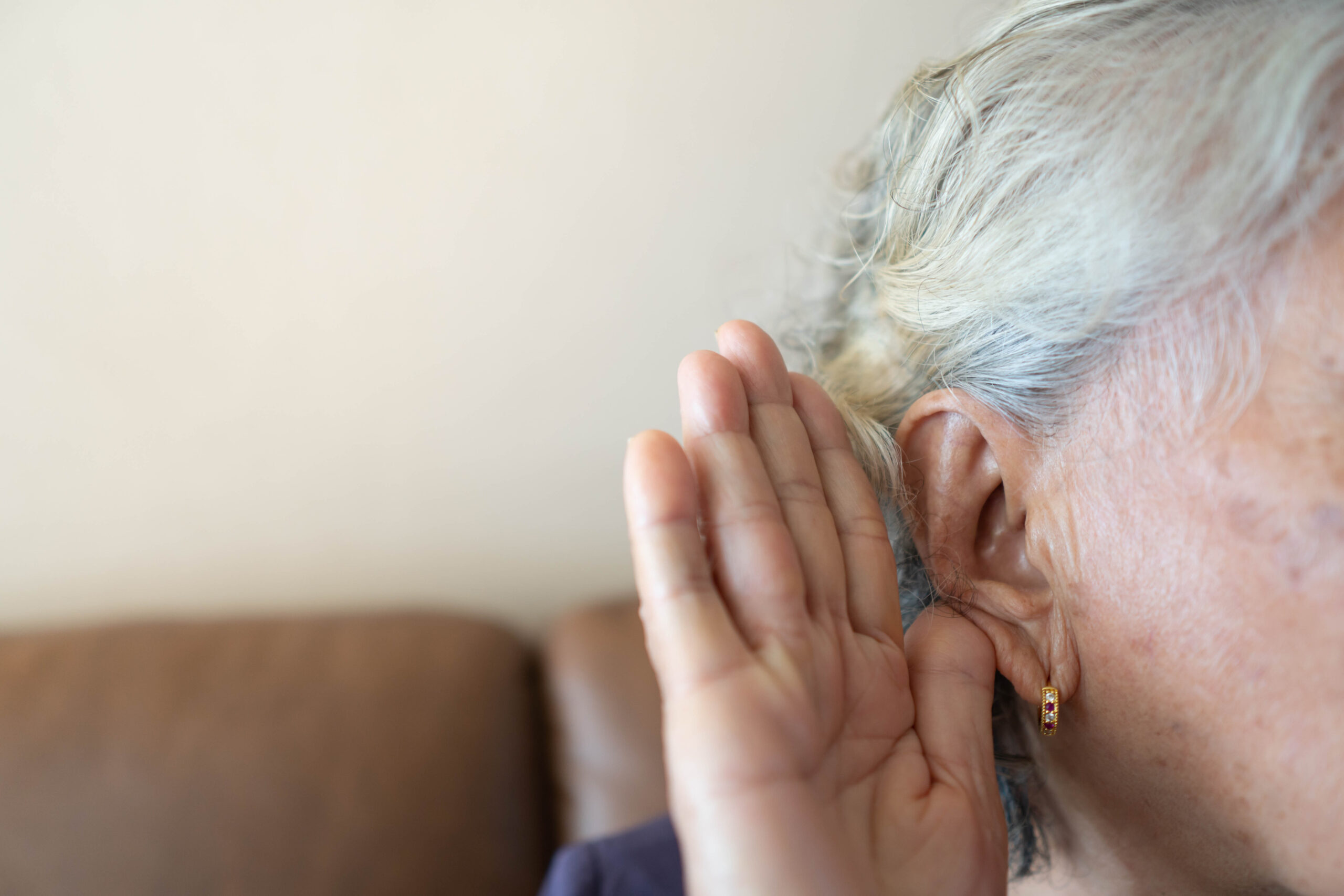 Hearing loss in seniors (Presbycusis) concept. Close up of elderly woman holding her hand near ear for trying hard to listen something. Elderly health care.