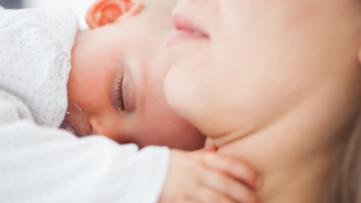 A deaf baby sleeps calmly on mother´s shoulder