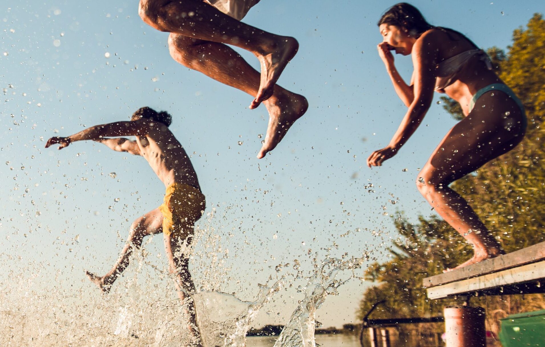 Friends having fun enjoying a summer day swimming and jumping at the lake.