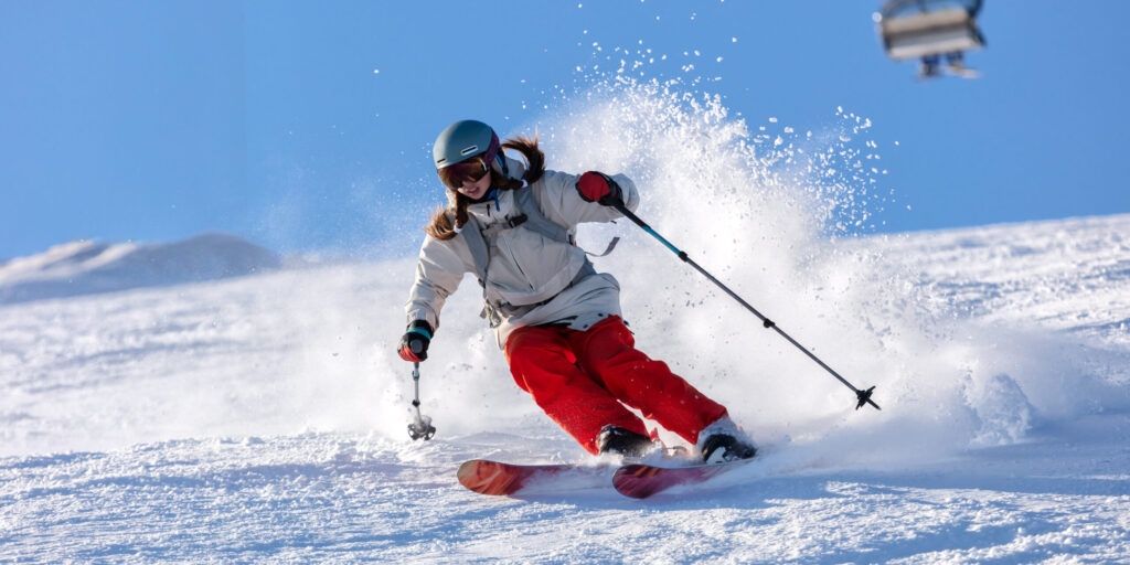 Junge Frau/Mädchen auf einer Skipiste, fährt Ski. Sie trägt eine rote Skihose und einen weißen Anorak.